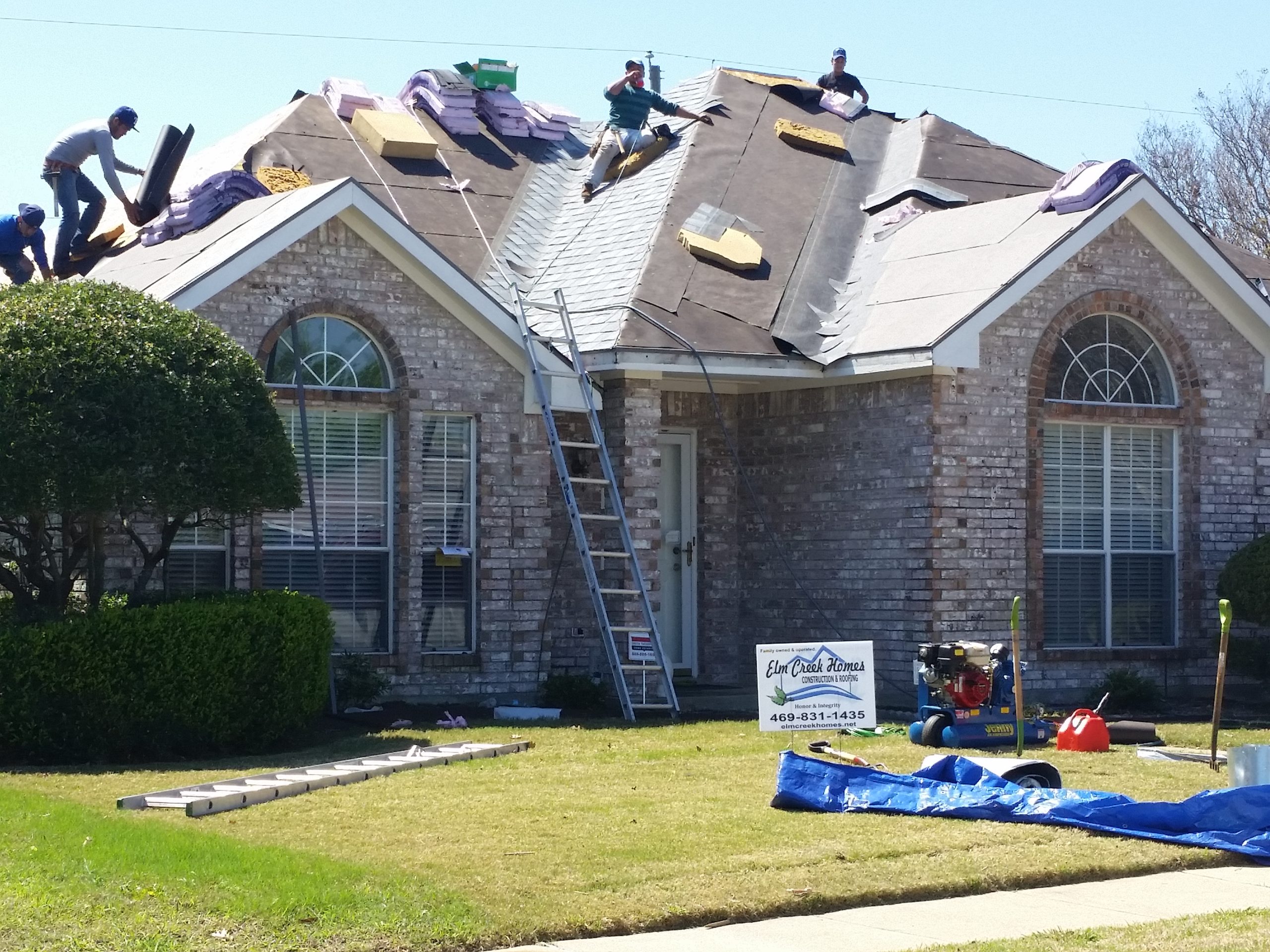 A team of roofers removing shingles from a damaged roof